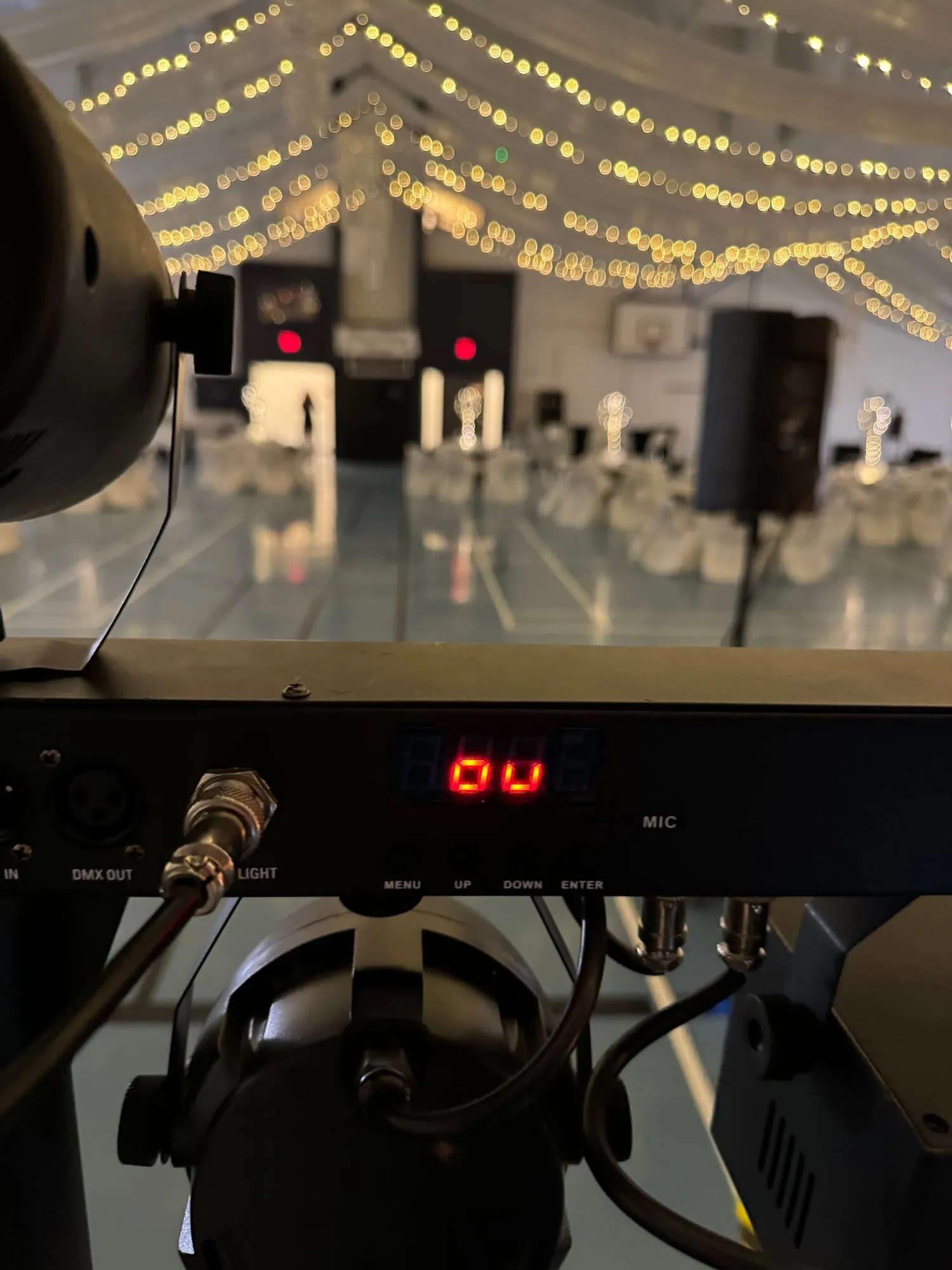 Ryan’s lighting rig and controller in the foreground of a hall strung with warm fairy lights, set up before an evening event