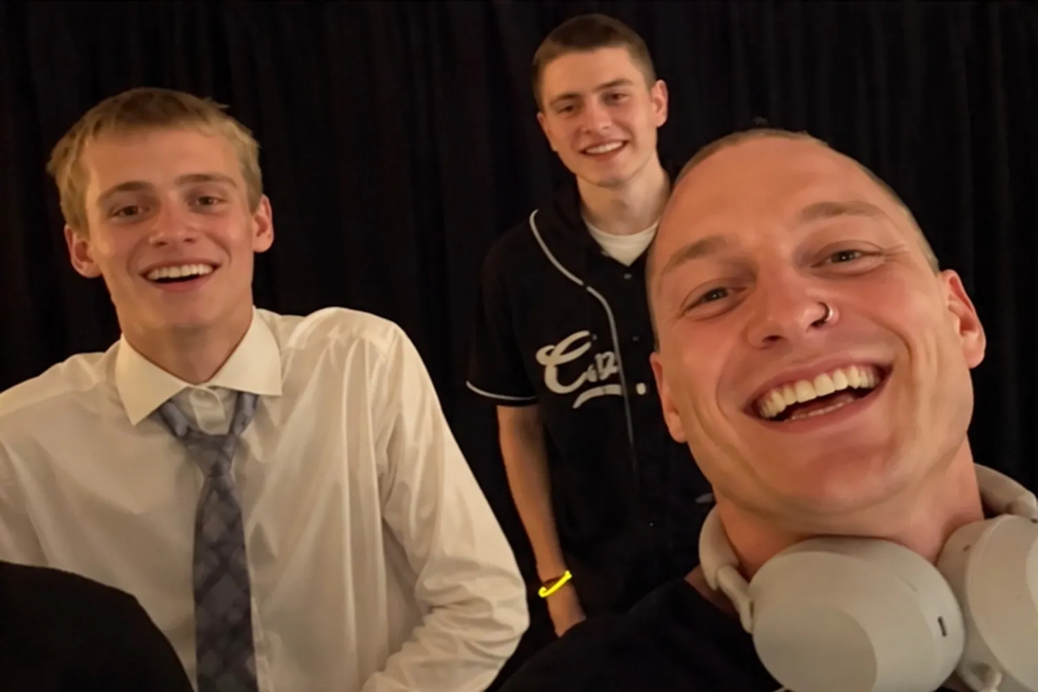 Ryan smiling at the camera with white headphones around his neck, two guests smiling behind him